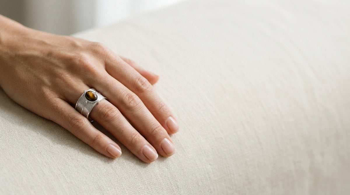 A hand wearing a sterling silver tiger's eye statement ring, resting on cream linen